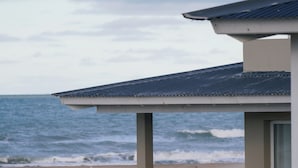 Una estructura junto a la playa con techo, banco y vista al océano.