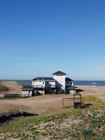 Un edificio costero de varios niveles y una torre destacada, situado en una playa de arena con una vista despejada del océano.