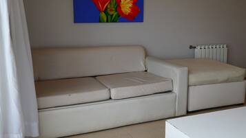 Un salon avec un canapé beige, un pouf marron, une table basse blanche et un tableau représentant des fleurs rouges accroché au mur.