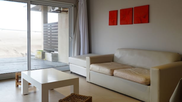 Una sala moderna con un sofá, una mesa de centro y un taburete pequeño. Hay un ventanal corredero que da a un espacio exterior.