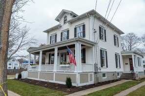 A two-story house with a porch, a flag, and a small front yard. - Downtown Mystic Getaway - Porch, Yard & Bunk Room (Mystic)