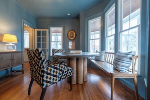 A dining area with a round table, patterned chairs, and a view through large windows. - Downtown Mystic Getaway - Porch, Yard & Bunk Room (Mystic)