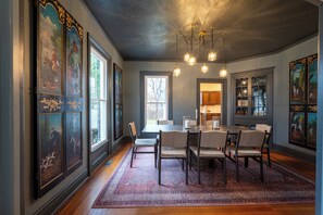 A dining area with a table and chairs, a chandelier, and artwork on the walls. - Downtown Mystic Getaway - Porch, Yard & Bunk Room (Mystic)