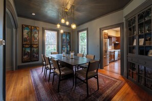 A dining room with a large table, chairs, and a chandelier. There are windows and a view of the outdoors. - Downtown Mystic Getaway - Porch, Yard & Bunk Room (Mystic)