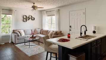 A modern kitchen with a central island, a dining area with a sofa and coffee table, and a ceiling fan.