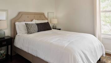 A neatly made bed with white bedding, a headboard, and two bedside lamps on a nightstand.