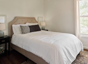 A neatly made bed with white bedding, a headboard, and two bedside lamps on a nightstand.