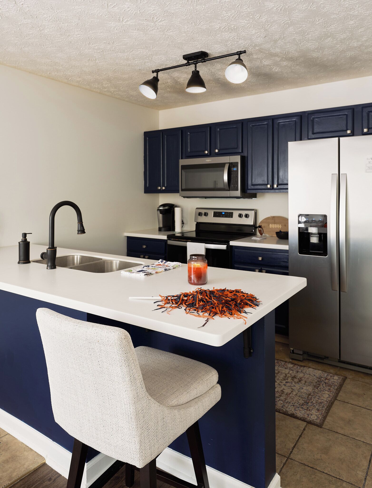 Una cocina moderna con una isla central, armarios azul oscuro, electrodomésticos de acero inoxidable y una silla blanca.