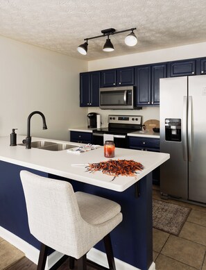 Una cocina moderna con una isla central, armarios azul oscuro, electrodomésticos de acero inoxidable y una silla blanca.