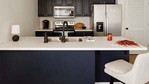 Eine moderne Küche mit dunklen Schränken, einem Edelstahlkühlschrank, einer Mikrowelle und einer Kaffeemaschine.