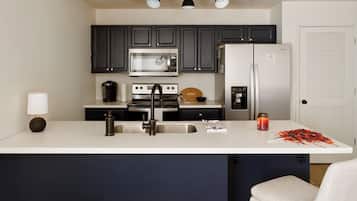A modern kitchen with dark cabinets, a stainless steel refrigerator, a microwave, and a coffee maker.