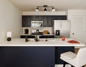A modern kitchen with dark cabinets, a stainless steel refrigerator, a microwave, and a coffee maker.