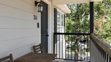 A covered porch with a wooden table and two chairs, a black metal railing, and a door with the number 201.