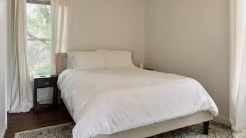 Un dormitorio con cama, mesita de noche, ventana con cortinas y una alfombra estampada.