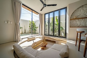 Ein modernes Wohnzimmer mit großem Fenster, Deckenventilator und Steinwand.