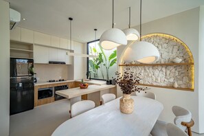 Eine moderne Küche mit Essbereich, ausgestattet mit einer Steinwand, Pendelleuchten und einem großen Fenster mit Pflanzen.