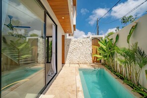 Una casa moderna con piscina, muro de piedra y plantas tropicales.