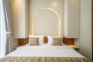 Ein Hotelzimmer mit einem Bett, zwei Nachttischen, einem Kopfteil mit Lampenaufsatz und einem Fenster mit Vorhängen.