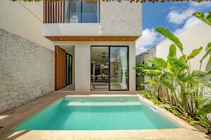 Ein modernes Haus mit Schwimmbad, Steinmauer und tropischer Bepflanzung.
