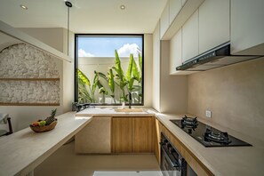 Une cuisine moderne avec un mur d’accent en pierre, une grande fenêtre agrémentée de plantes et une cuisinière intégrée.