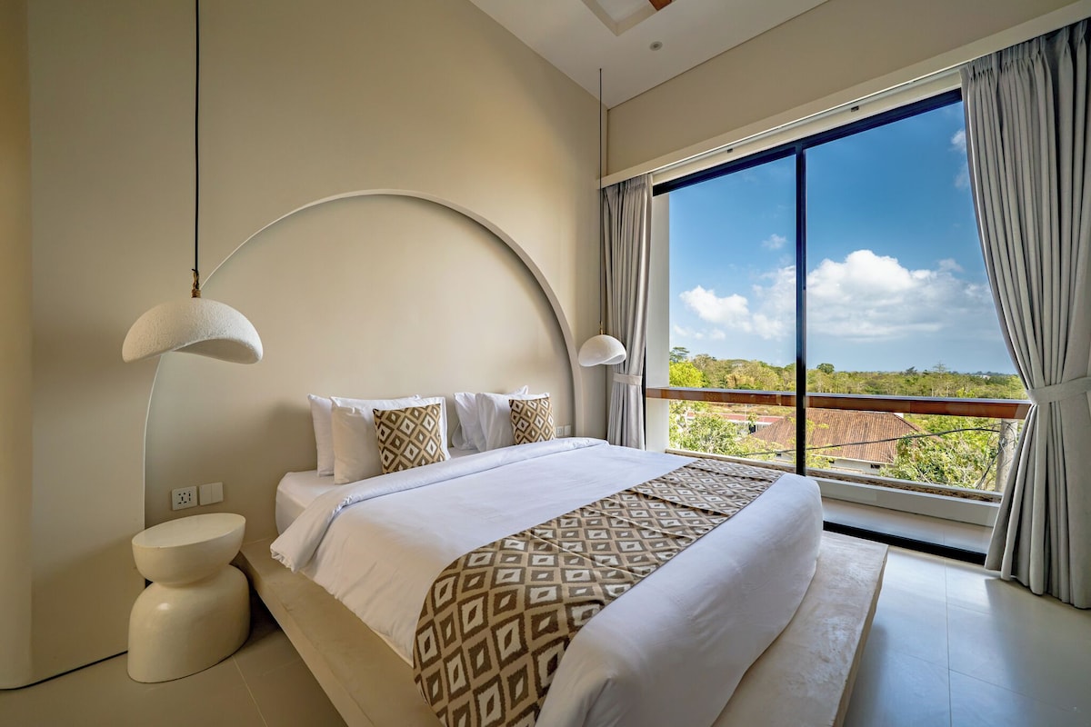 Ein Schlafzimmer mit einem großen Bett, einer gewölbten Wand, einem Balkon mit Aussicht und einer modernen Deckenleuchte.