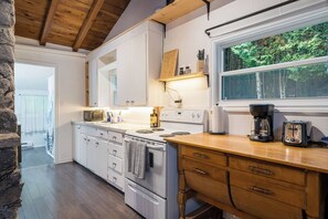 A kitchen with white cabinets, a wooden countertop, a stove, and a window overlooking greenery.