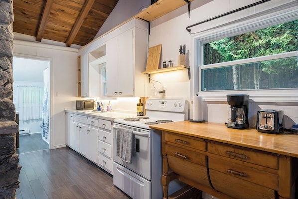 A kitchen with white cabinets, a wooden countertop, a stove, and a window overlooking greenery.