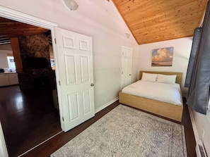 A bedroom with a bed, a stone fireplace, and a view of the living area.