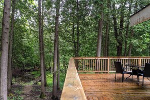 Une terrasse en bois avec une table et des chaises, entourée de grands arbres.