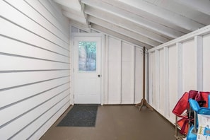 A covered porch with a door, a wooden chair, and a red and blue bag.
