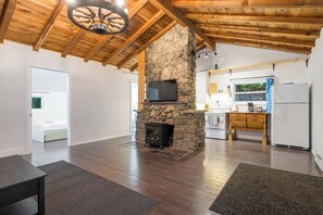 A spacious living area with a stone fireplace, a television mounted on the wall, and a kitchen with modern appliances.