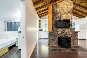 A modern interior with a stone fireplace, a bed, and a kitchen in the background.
