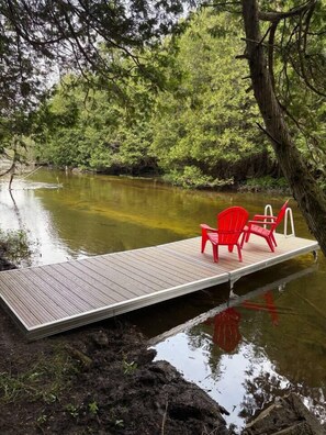 A wooden dock extending into a body of water with two red chairs and a white railing.