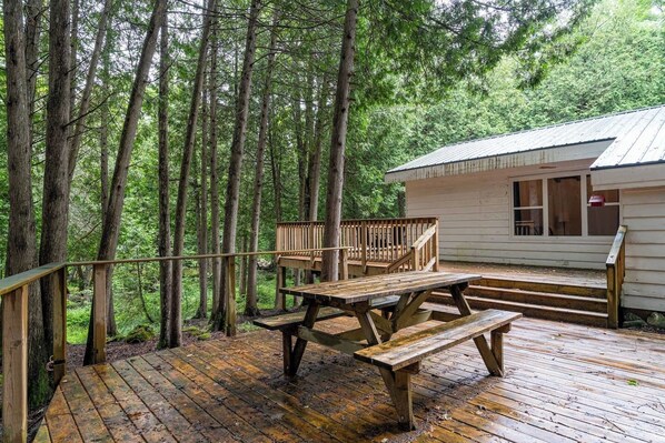A wooden deck with picnic tables and a railing overlooking a forested area.