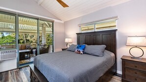 Une chambre à coucher avec un grand lit, un ventilateur de plafond, une table de chevet et une fenêtre donnant sur un paysage verdoyant.
