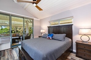 Ein Schlafzimmer mit einem großen Bett, einem Deckenventilator, einem Nachttisch und einem Fenster mit Blick auf Grünflächen.