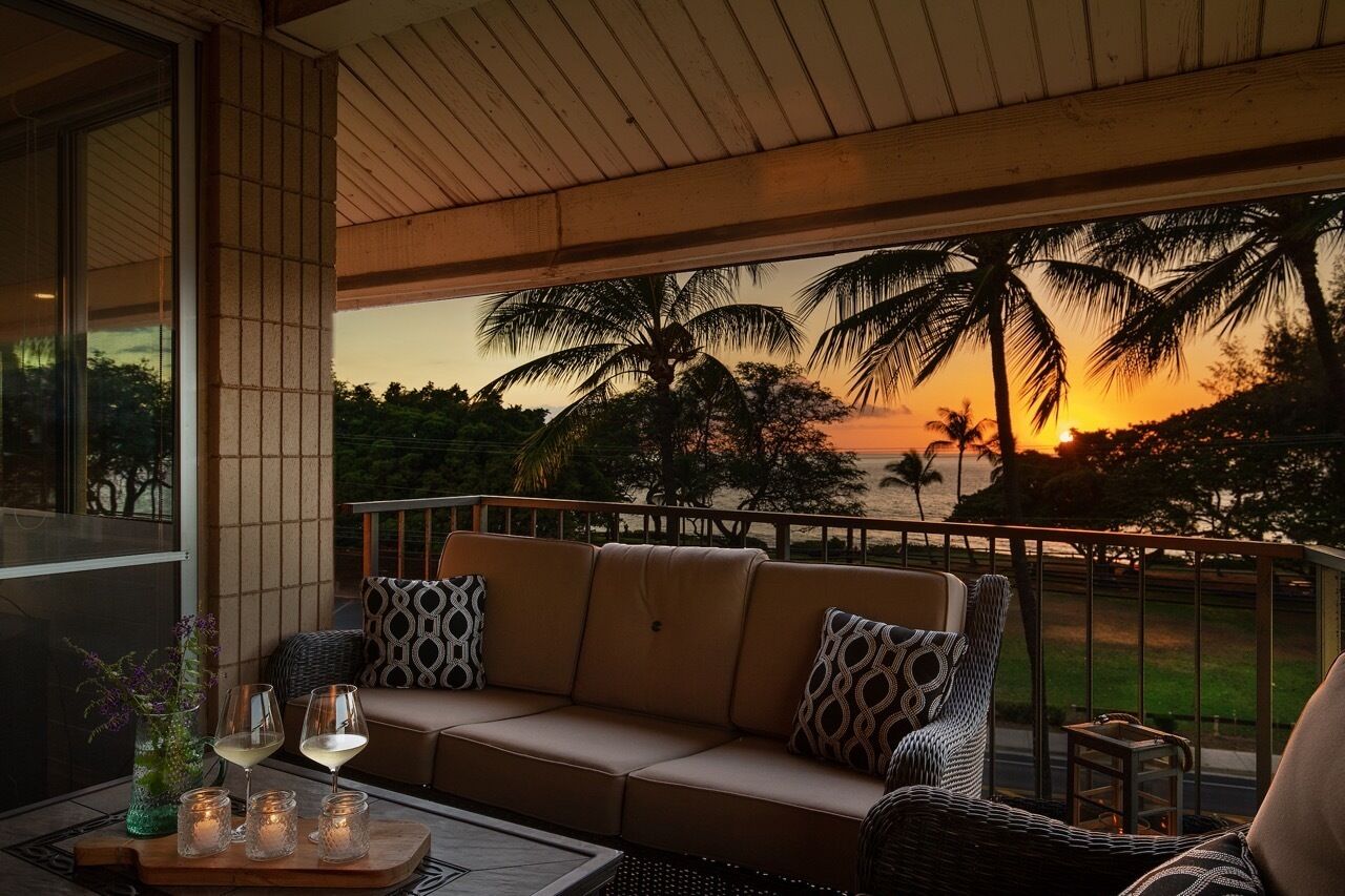 A balcony with a sofa, cushions, and a table with candles and glasses.