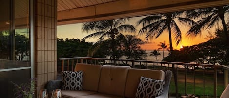 A balcony with a sofa, cushions, and a table with candles and glasses.