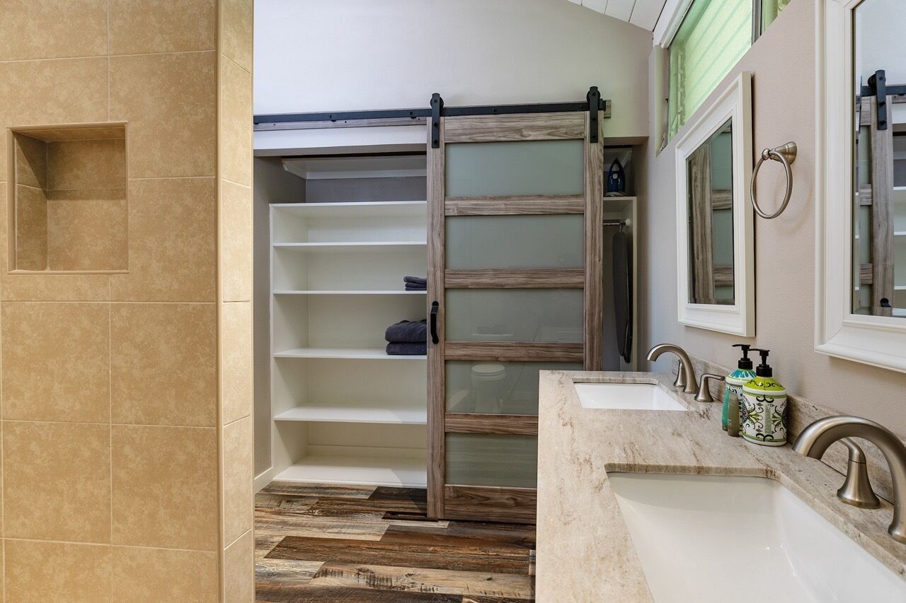 A bathroom with a sliding door closet, a sink with a mirror, and a vanity with toiletries.