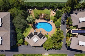 Eine Vogelperspektive zeigt eine Wohngegend mit einem Swimmingpool, umgeben von üppiger Vegetation, Solaranlagen und einer kleinen Terrassenfläche.