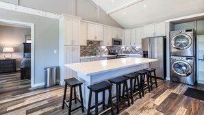 Une cuisine moderne dotée d’un grand îlot central, d’appareils électroménagers en acier inoxydable et d’un revêtement de sol imitant le bois.