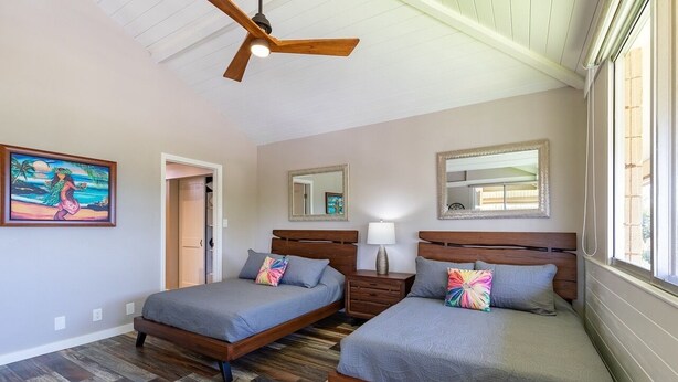 Une chambre avec deux lits, des têtes de lit en bois, un ventilateur de plafond et un tableau au mur.