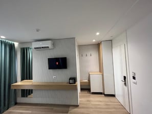 A modern hotel room with a flat-screen TV mounted on the wall, a wooden bench, a small table, and a wardrobe. - Hotel Ilio (Ksamil)