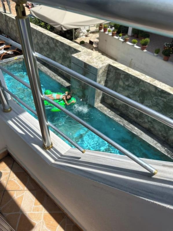 A swimming pool with a person in a green swimsuit, surrounded by a metal railing and potted plants. - Hotel Ilio (Ksamil)