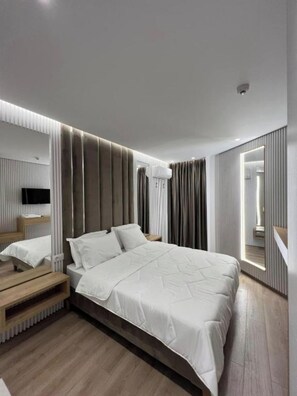 Een moderne slaapkamer met een groot bed, een houten bankje, een televisie en een spiegel.