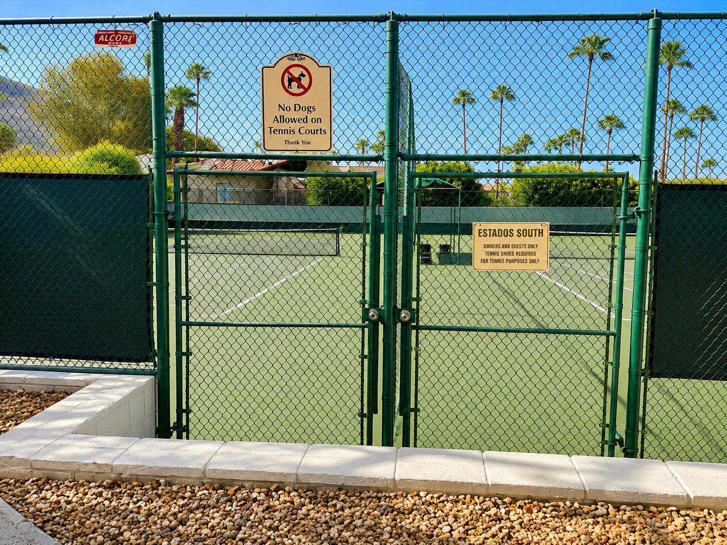 Een tennisbaan met een hekken en borden: 'Honden niet toegestaan' en 'Tennisschoenen verplicht'.