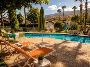 A swimming pool area with lounge chairs and umbrellas, surrounded by palm trees and a mountain backdrop. - Modern  1-bedroom condo with AC in sunny Palm Springs (Palm Springs)