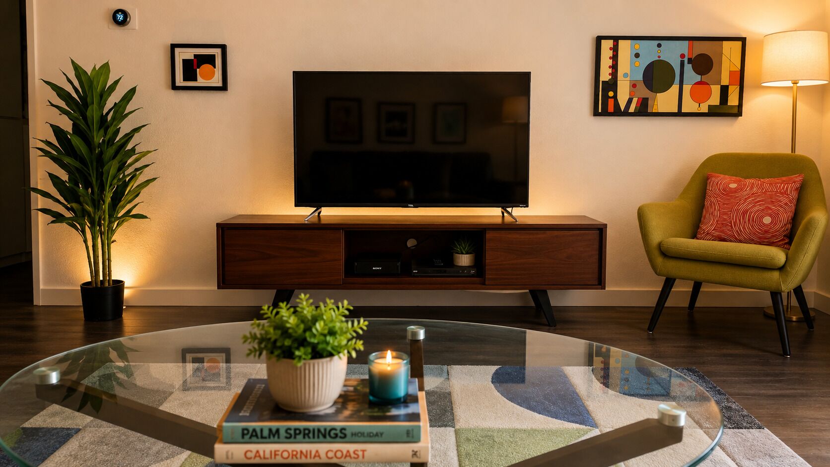 A modern living room with a glass coffee table, a flat-screen TV, a potted plant, a bookshelf, and a yellow armchair.