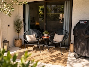 An outdoor seating area with two wicker chairs, a small table, a potted plant, and a barbecue grill. - Modern  1-bedroom condo with AC in sunny Palm Springs (Palm Springs)