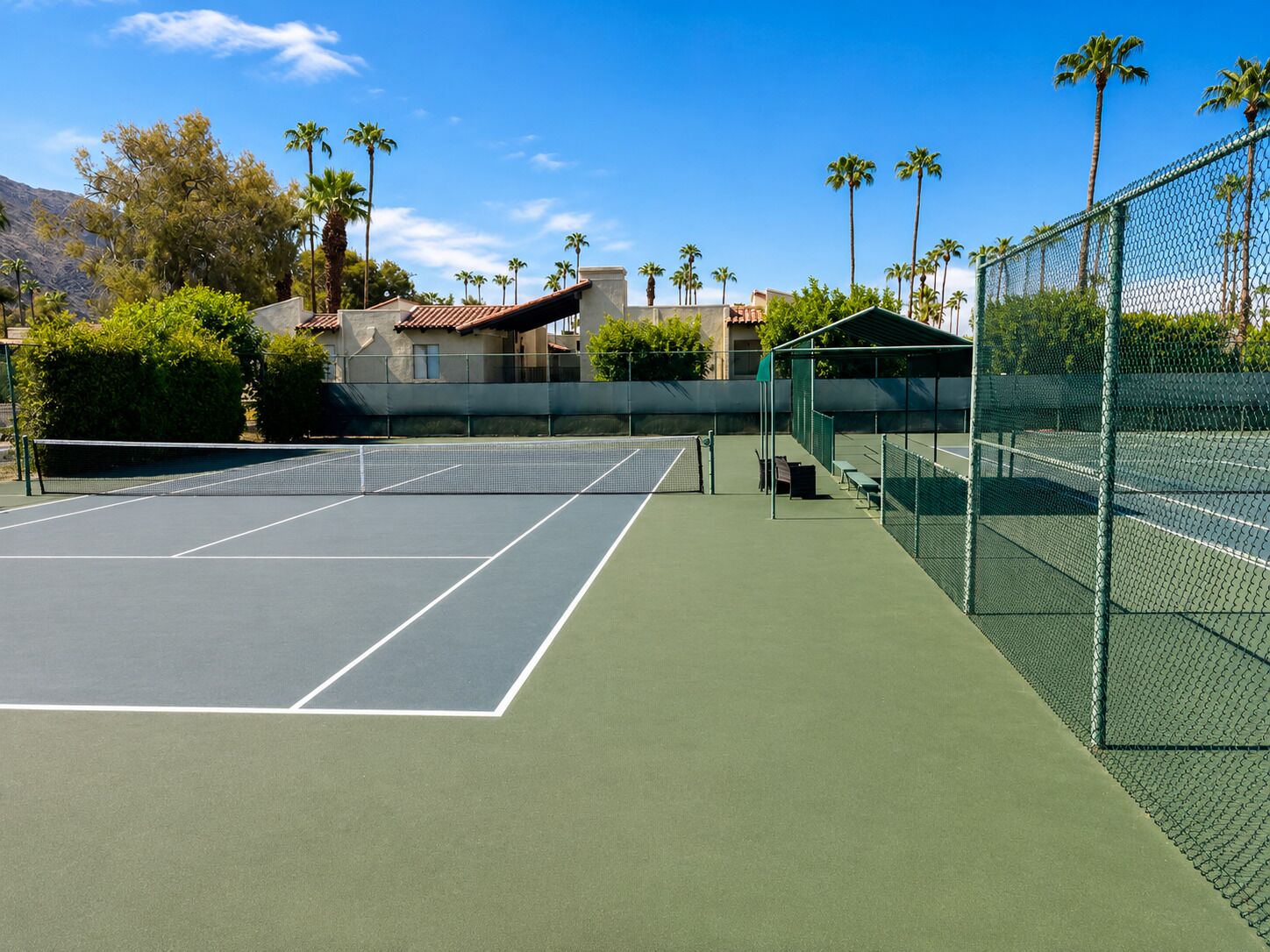 Un court de tennis avec un filet, des bancs et un espace de repos couvert.